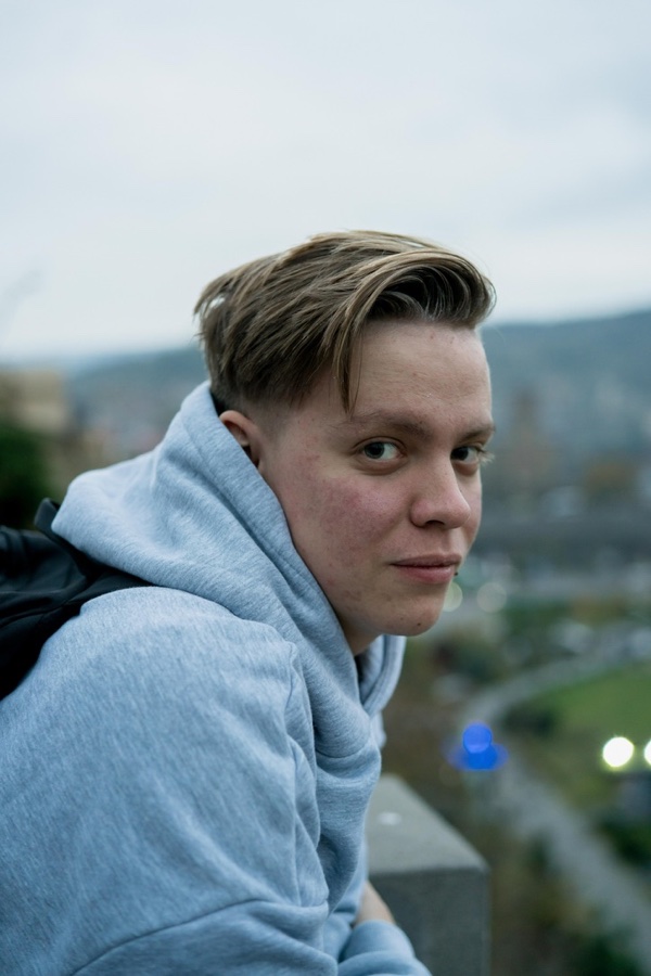 Artem Efremenko in a grey hoodie, leaning on a railing above a city at dusk and looking back at the camera.