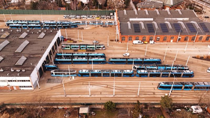 Aerial view of a tram depot yard with rows of blue trams in front of a brick shed with solar panels.
