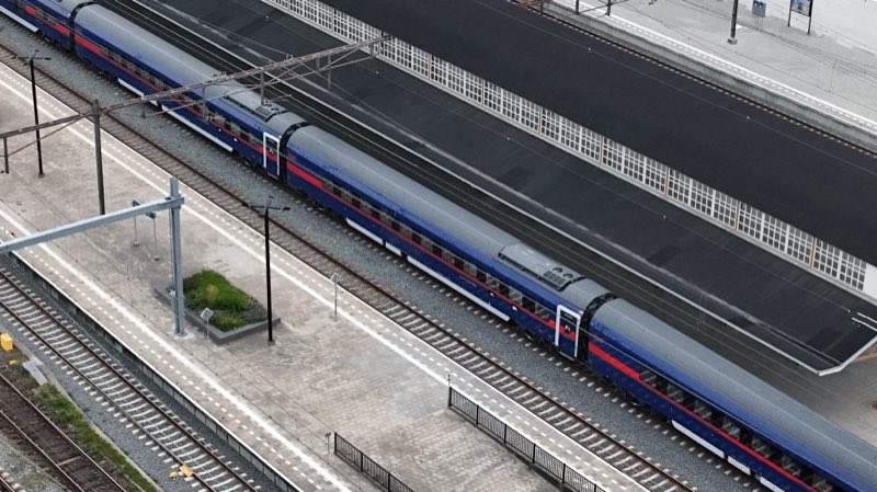 Blue night train with a red stripe standing at an empty station platform, seen from above.