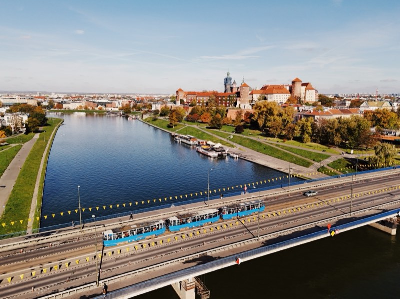 Blue tram crossing a bridge over the Vistula, with Wawel Castle on the far bank.