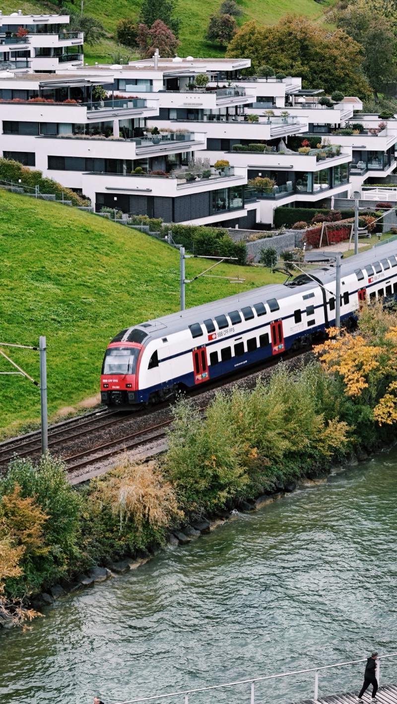 Double-deck train passing along the water below terraced modern houses.