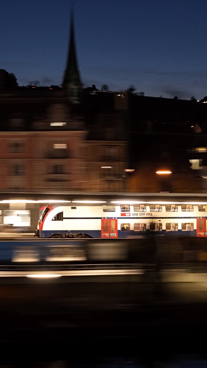 Double-deck train passing at night below a church spire.