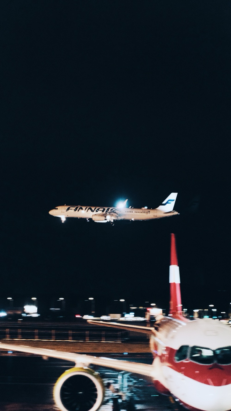 A Finnair jet landing at night, seen past the wing and tail of a parked aircraft.