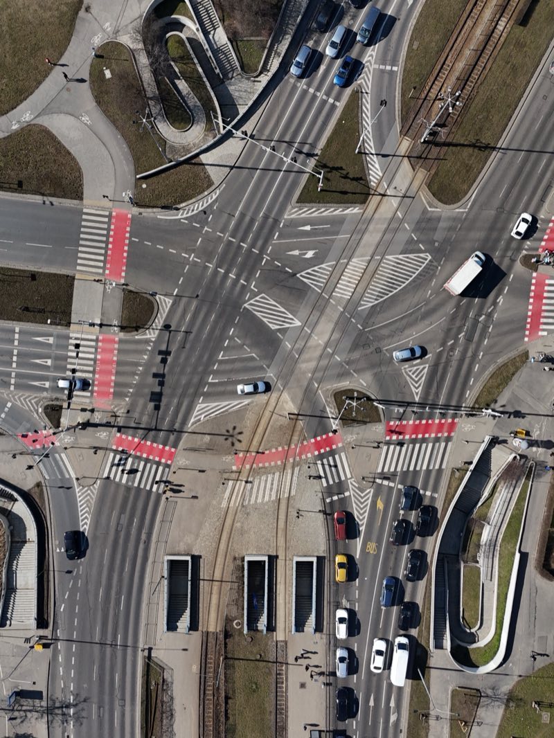 Large road junction with tram tracks and red crossings, seen from directly above.