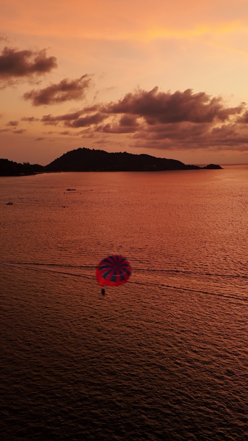 Parasail over the sea at sunset, with an island on the horizon.