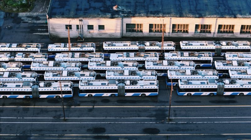 Rows of white and blue trolleybuses parked in front of a long depot shed.