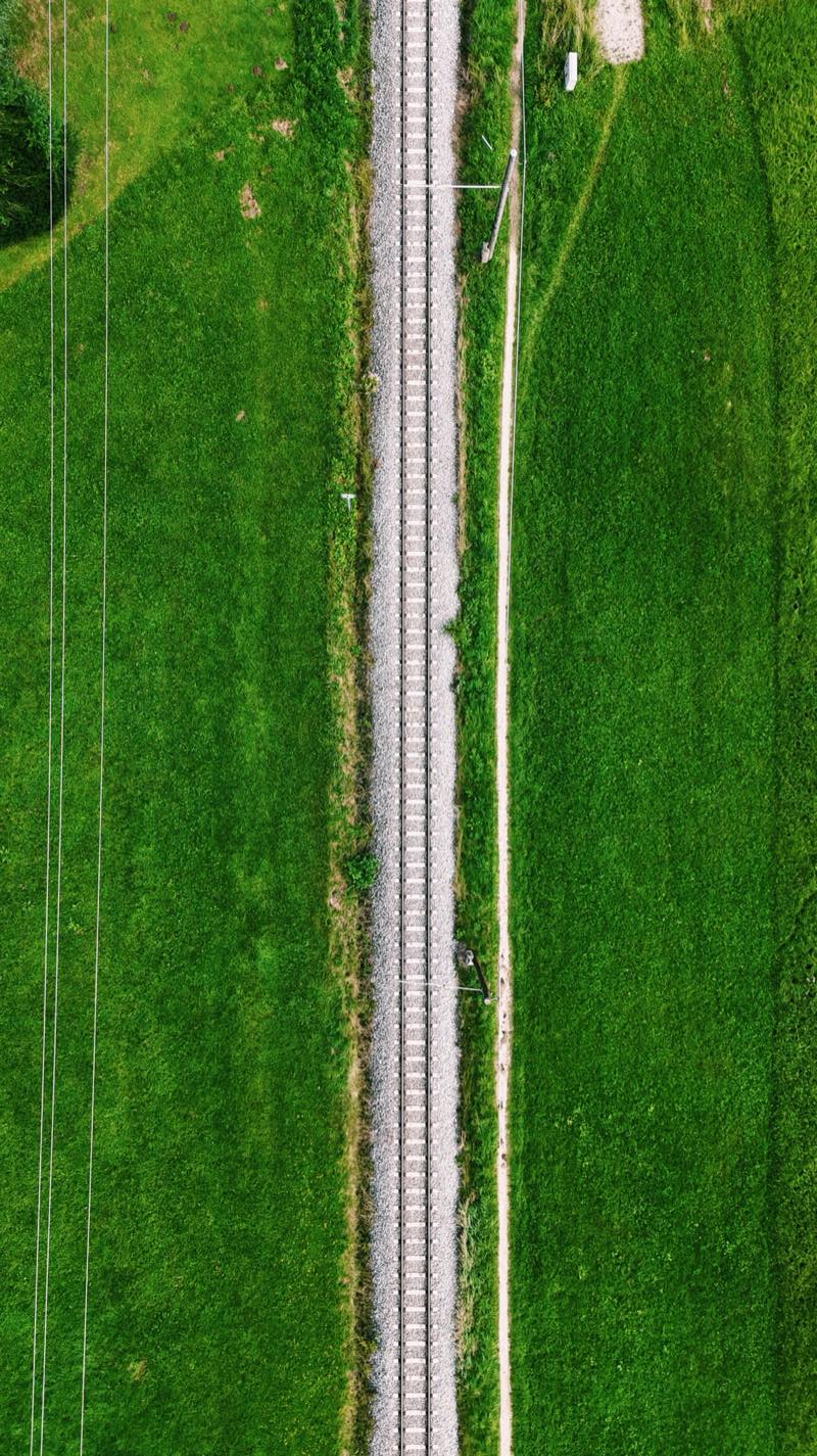 Single railway track running straight between two green fields, seen from directly above.