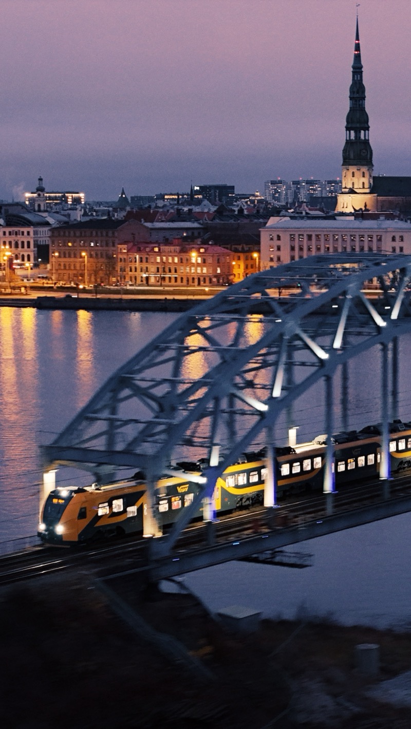 Steel arch railway bridge at dusk, with a church spire and the old town lit up behind.
