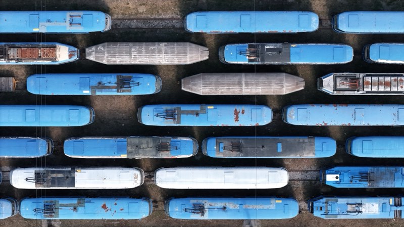 Top-down view of old blue and white tram roofs in staggered rows, some stripped and rusting.