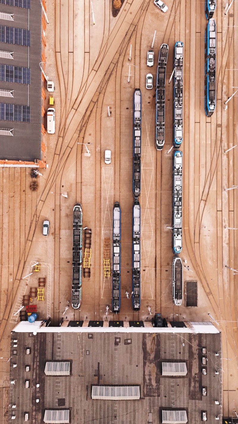Top-down view of a tram depot yard: parked trams, fanning tracks and the roof of the shed.