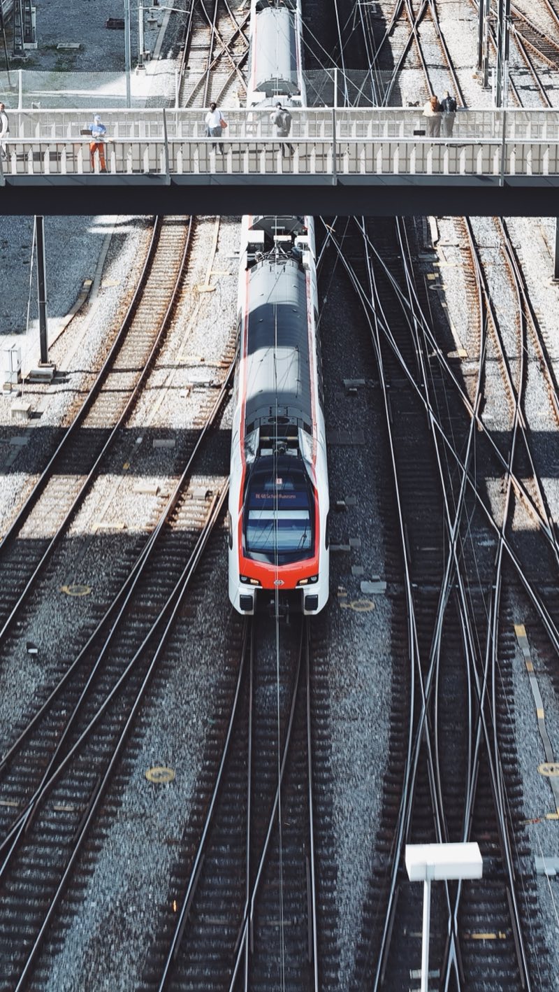Train approaching under a footbridge across a wide fan of tracks.