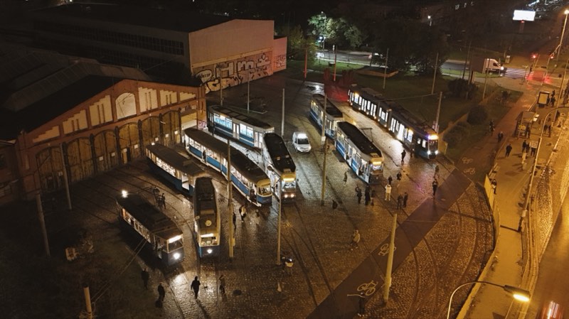 Tram depot at night, trams parked under lights beside a brick shed with arched windows.