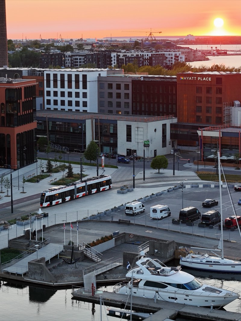 Tram running along a harbour front at sunset, yachts moored below.
