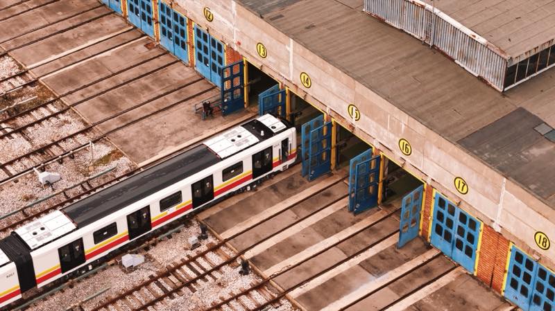 White metro train entering a depot shed with numbered doors.