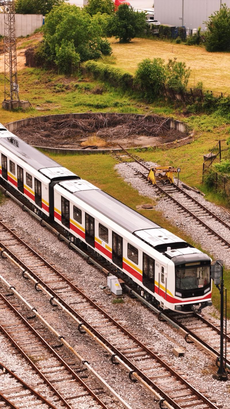 White metro train with red and yellow stripes on depot tracks.